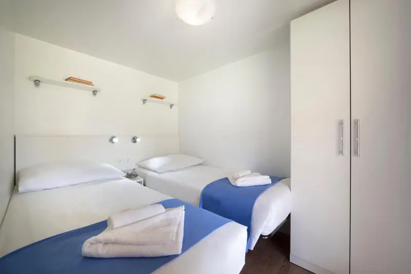 Une chambre lumineuse avec deux lits simples et une armoire blanche.