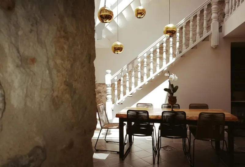Une table en bois est entourée de chaises noires dans un espace lumineux avec un escalier.