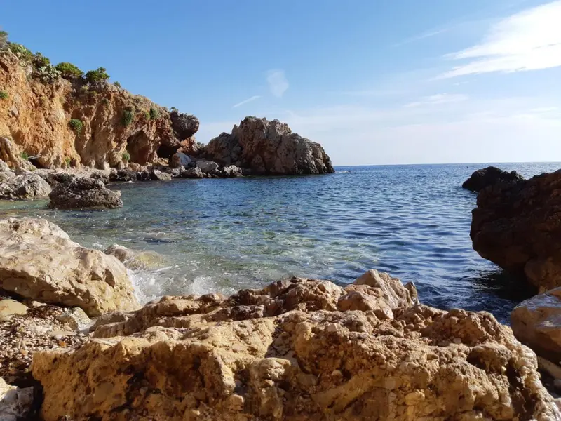 Une crique rocheuse s'ouvre sur une mer bleue et calme.