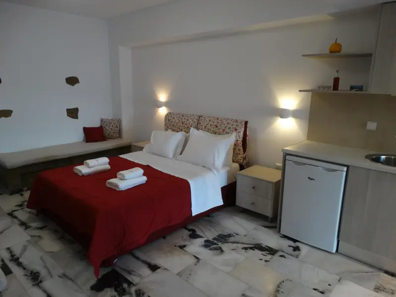 Une chambre lumineuse avec un lit recouvert d'une courtepointe rouge et un petit réfrigérateur.