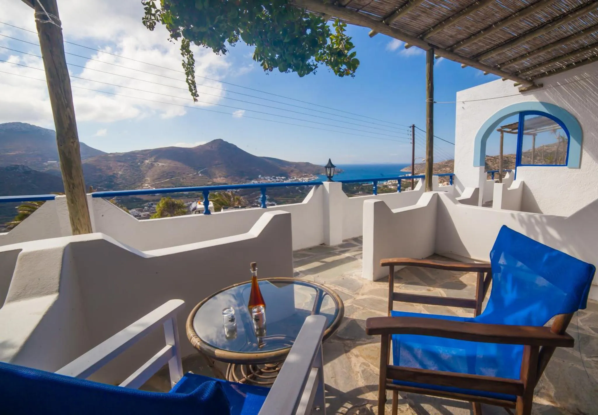 Terrasse avec table et chaises offrant une vue sur la mer et les montagnes.