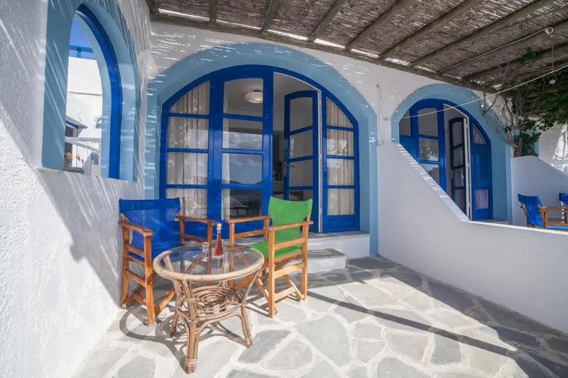 Terrasse ombragée avec mobilier en osier et vue sur des ouvertures bleues.