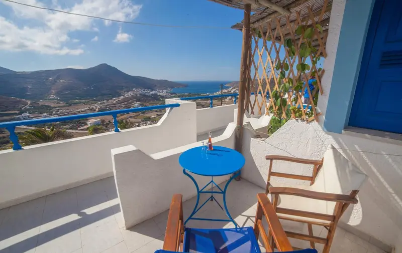 Terrasse avec table et chaises offrant une vue sur la mer et les montagnes.