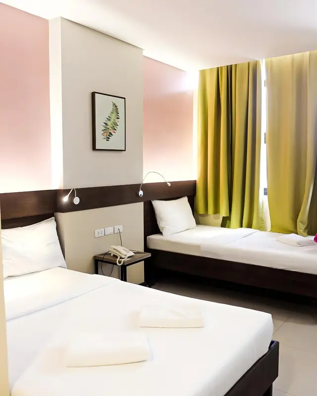 Chambre lumineuse avec deux lits simples et une décoration murale.