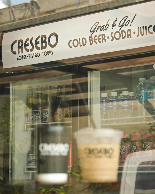 Une vitrine de commerce affiche des bouteilles et une personne tenant une boisson.