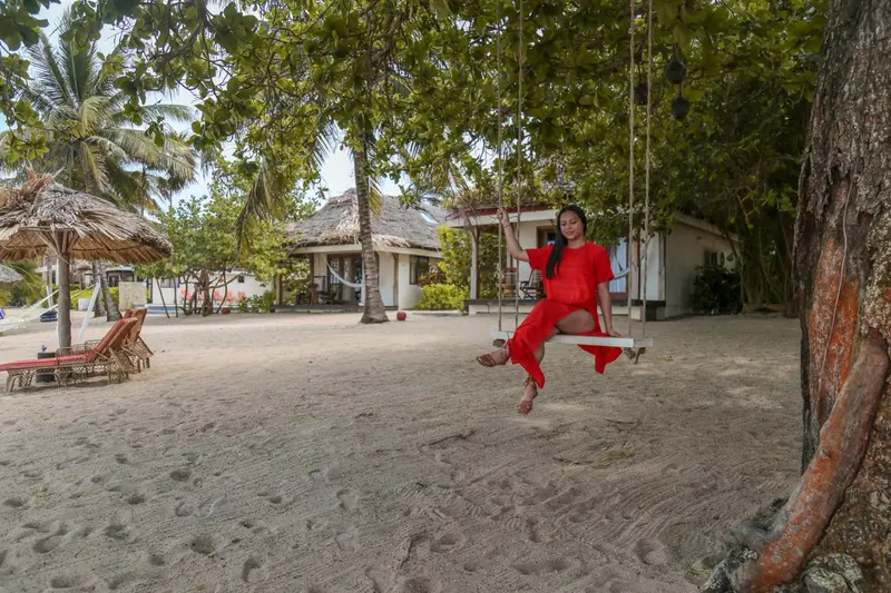 Une femme se balance sur une balançoire en bois au milieu d'une plage de sable blanc.