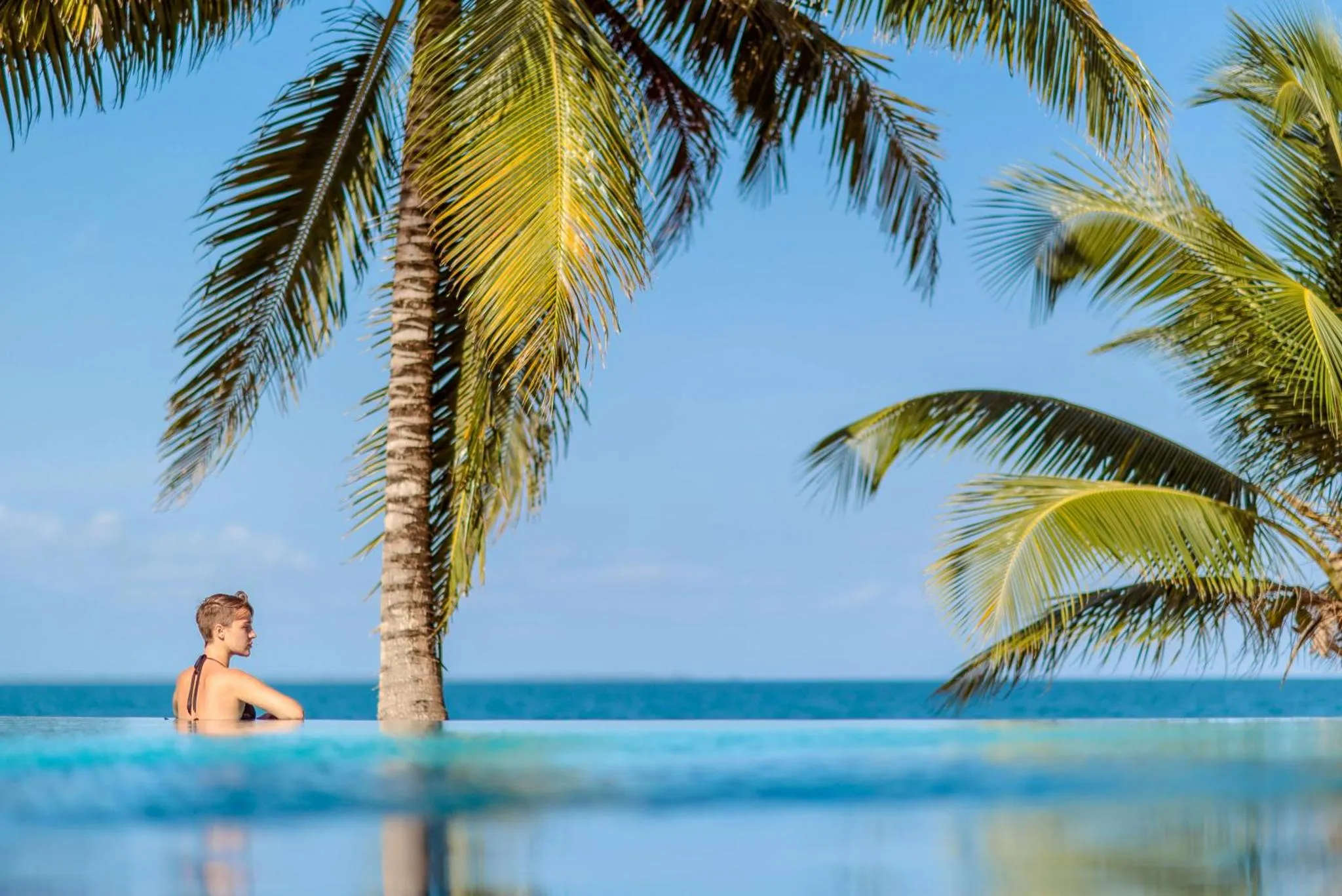 Une personne est assise au bord d'une piscine à débordement avec vue sur la mer.