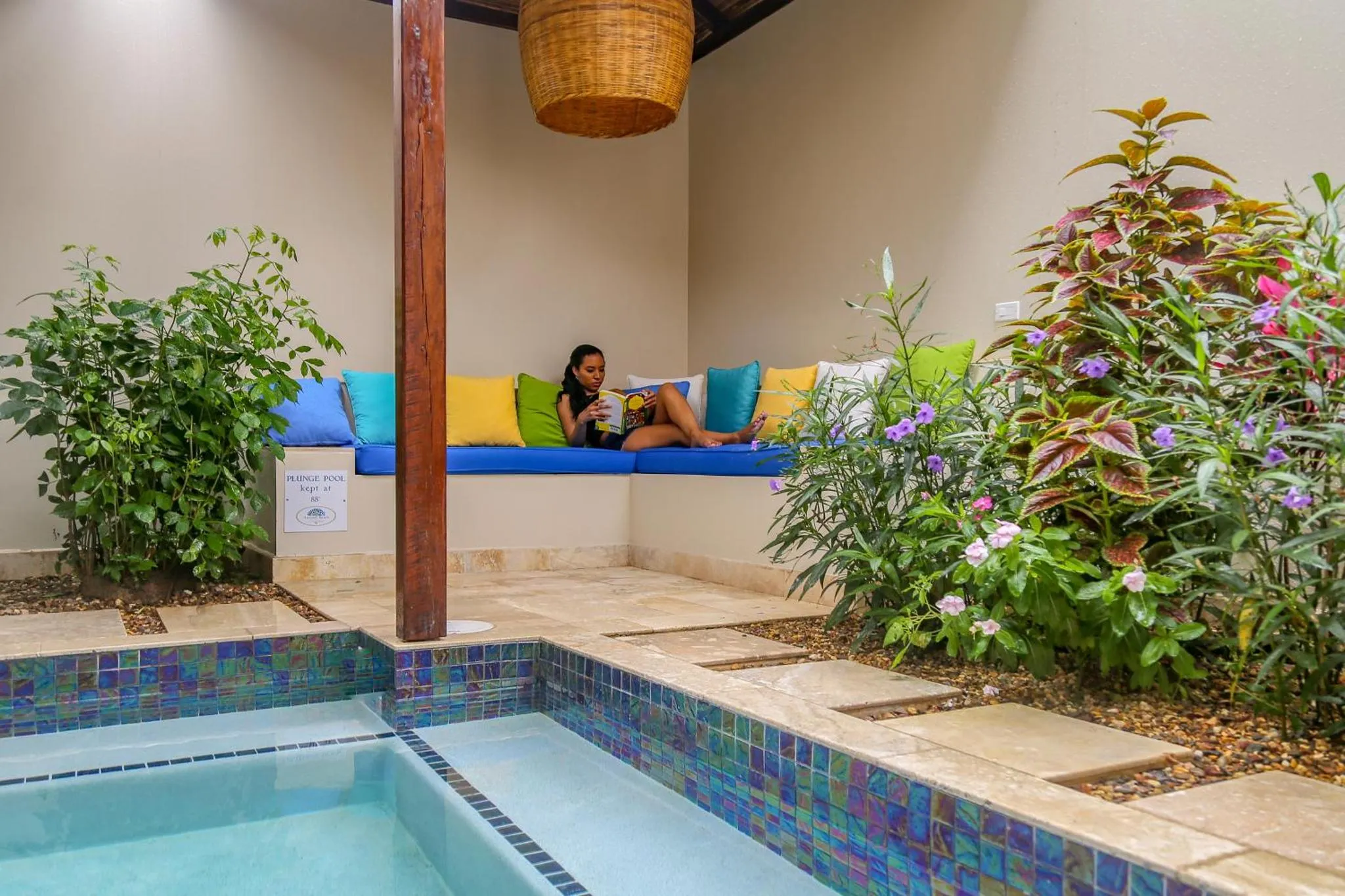 Une personne se repose sur un banc coloré près d'une piscine et d'une végétation luxuriante.