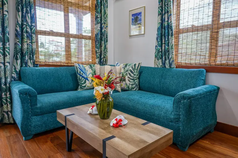 Un canapé bleu turquoise et une table basse en bois sont disposés devant de grandes fenêtres.