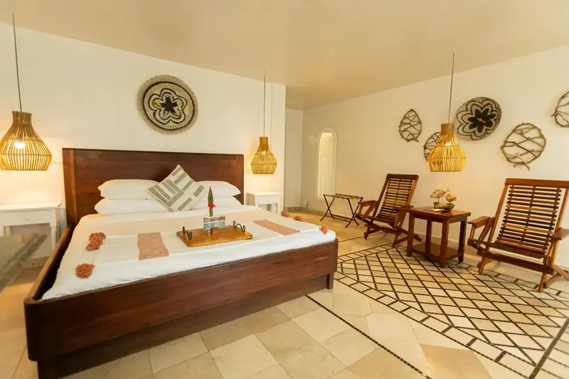 Une chambre lumineuse avec un grand lit et deux fauteuils en bois.