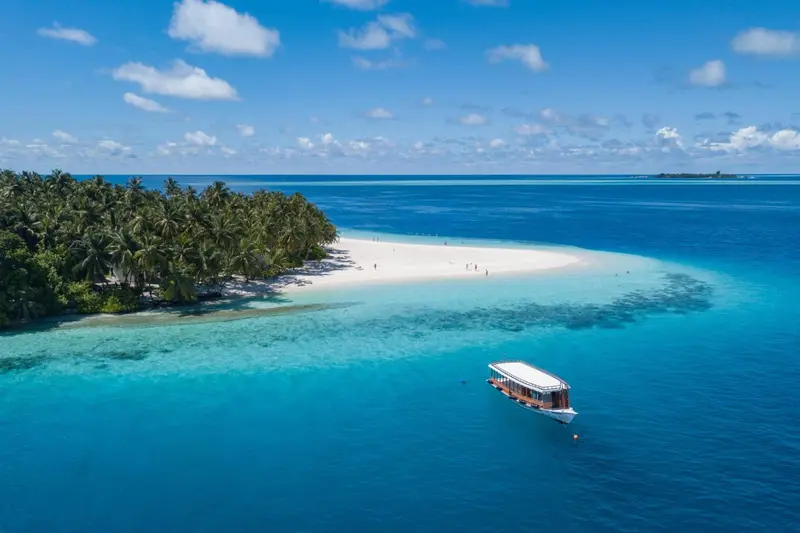 Vue aérienne d'une île tropicale avec une plage de sable blanc et un bateau en mer.