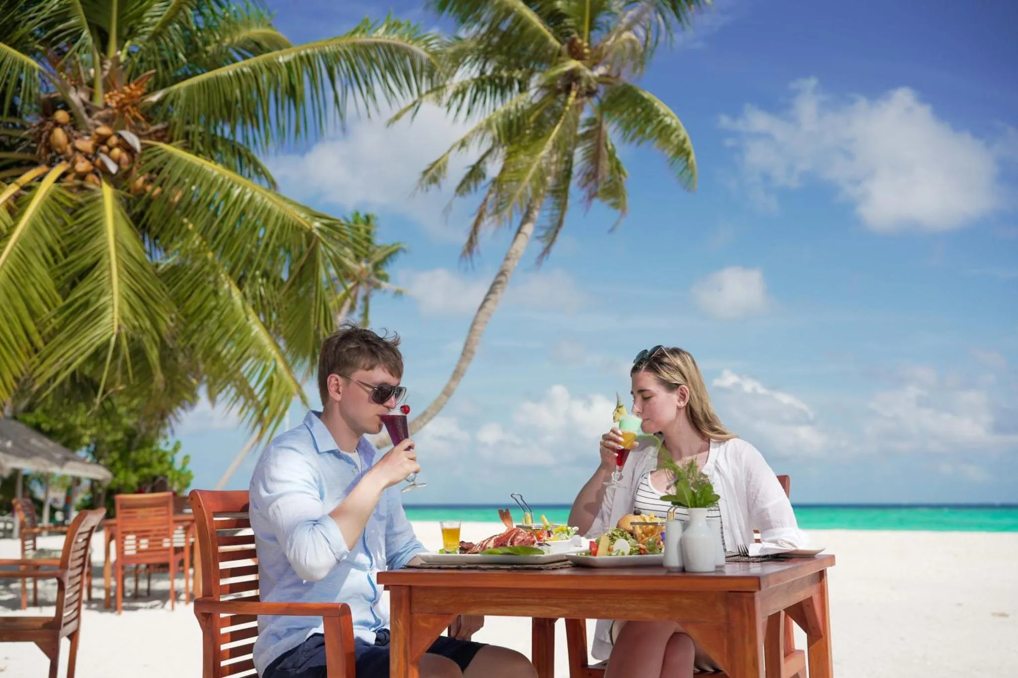 Un couple déguste des boissons et un repas sur une table en bord de mer.