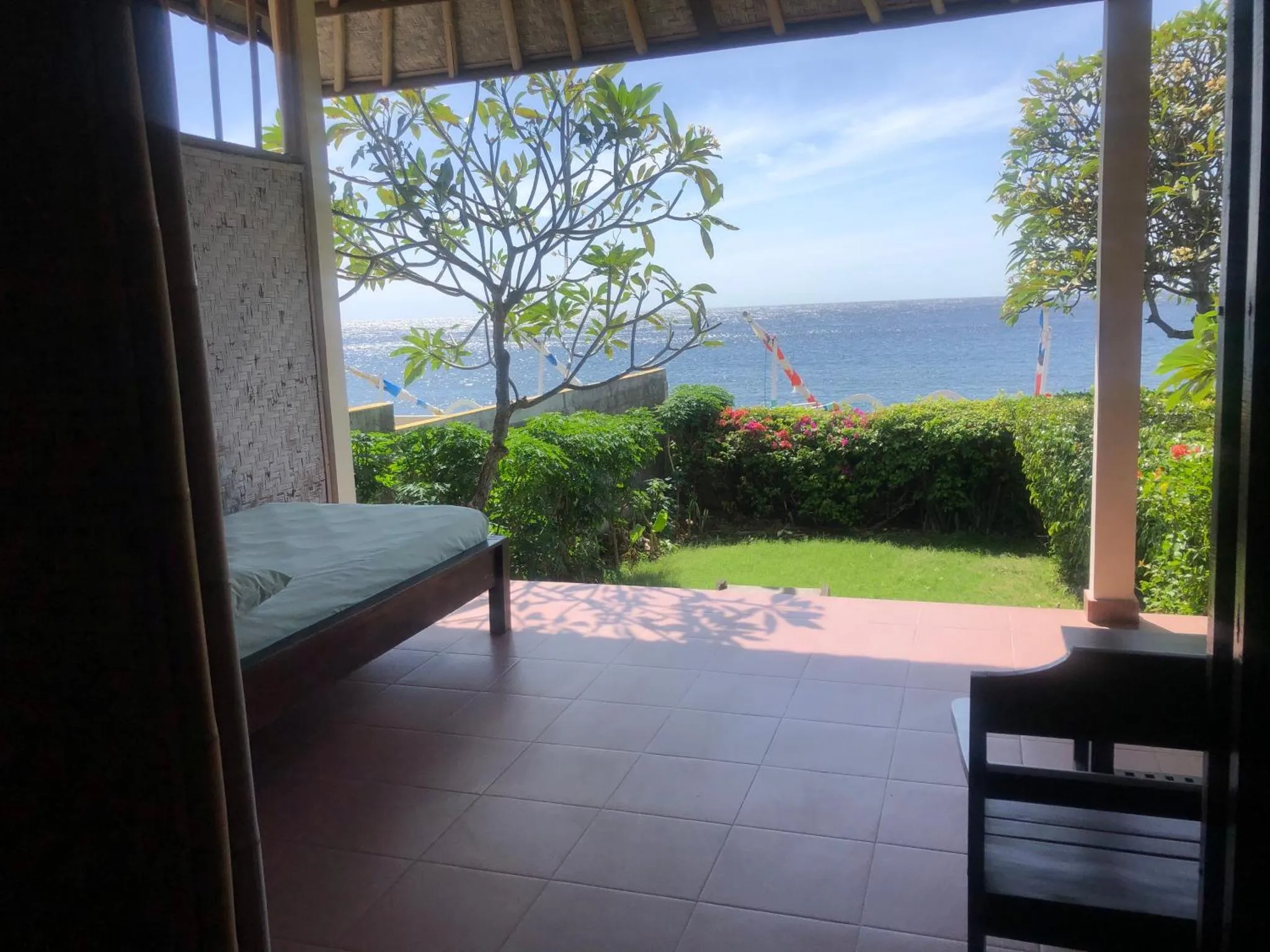 Vue sur la mer depuis une terrasse ombragée avec un lit.