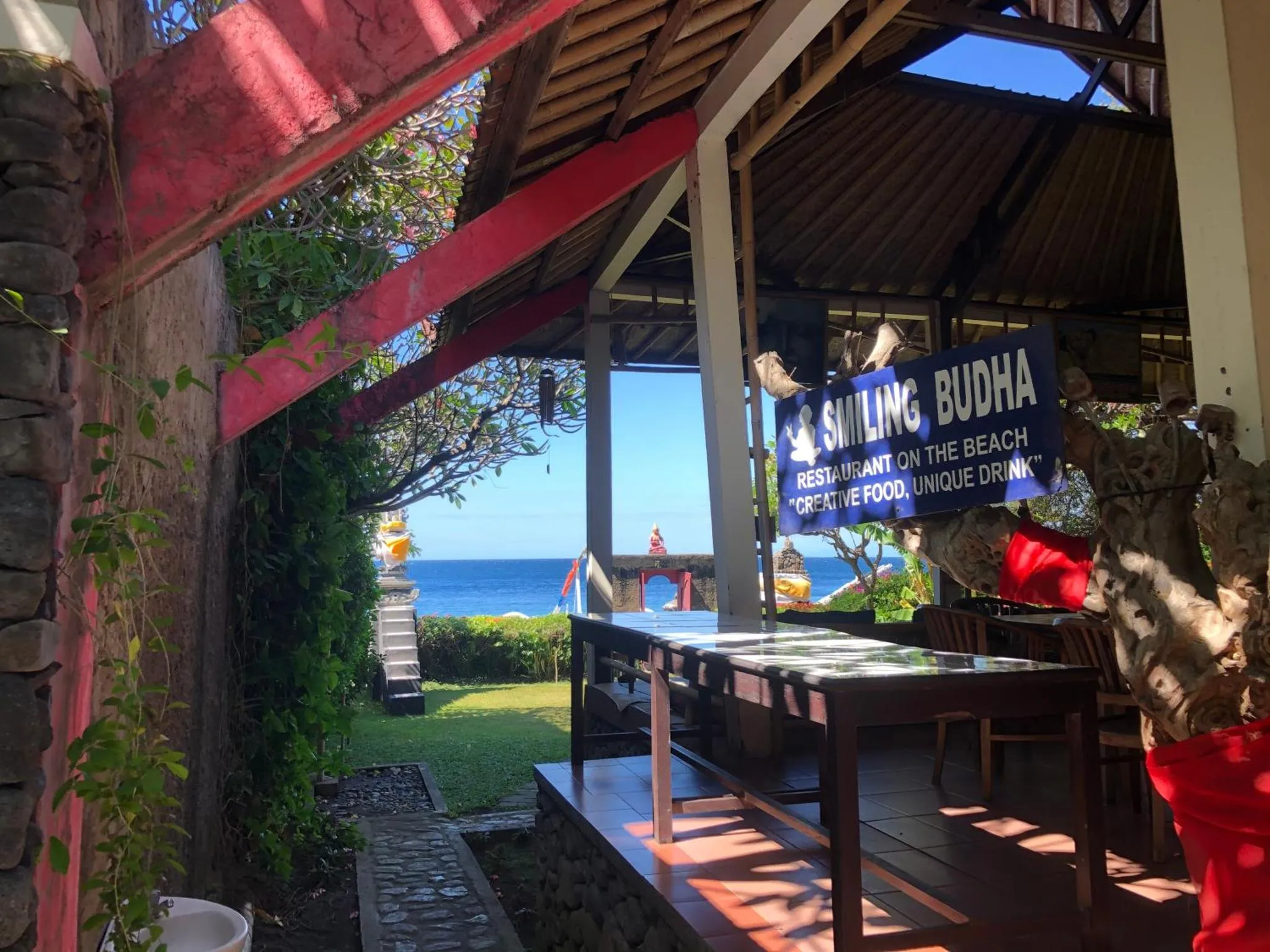 Tables en bois disposées sur une terrasse ombragée avec vue sur la mer.