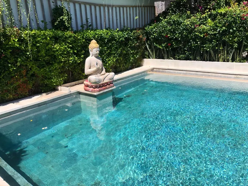 Une statue de Bouddha orne le bord d'une piscine carree turquoise.