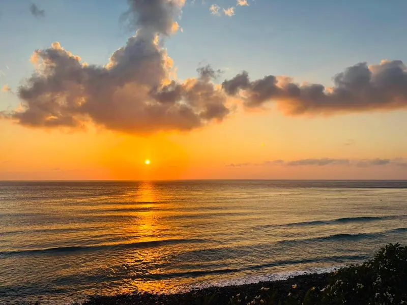 Coucher de soleil sur l'océan avec un ciel nuageux et une plage en contrebas.