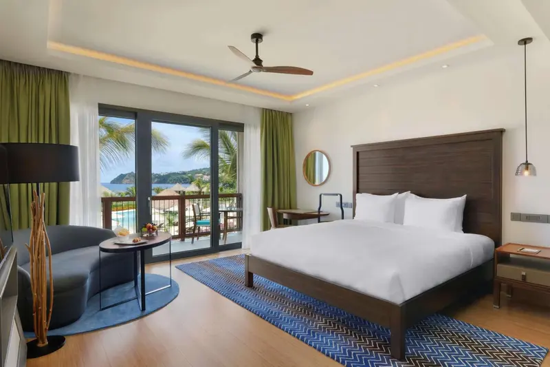 Chambre lumineuse avec un grand lit et un accès à une terrasse offrant une vue sur la mer.