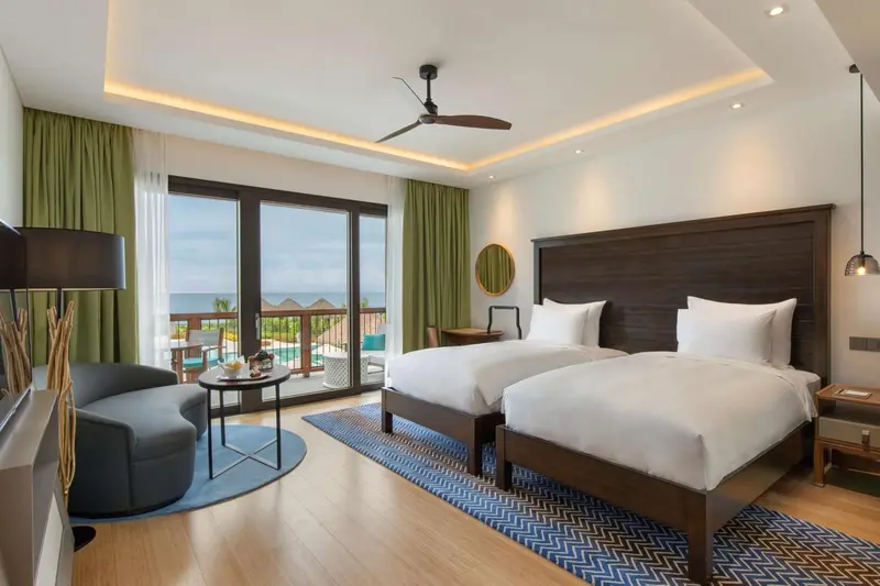 Chambre lumineuse avec deux lits simples et vue sur la mer.