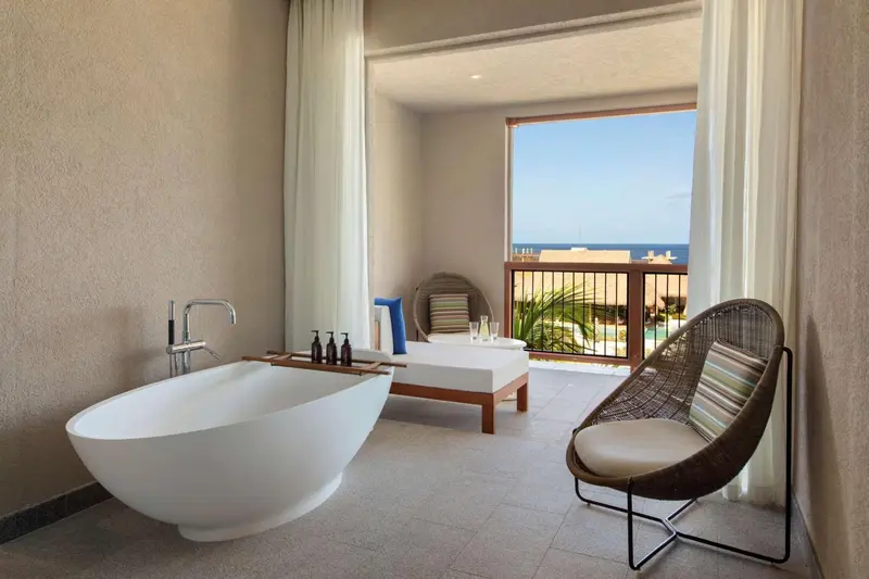 Une baignoire blanche se trouve dans une salle de bain lumineuse donnant sur une terrasse.