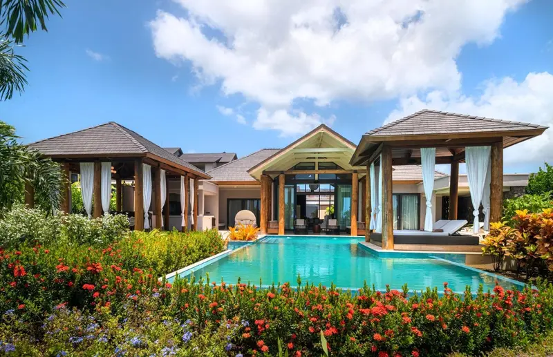 Villa avec piscine et végétation luxuriante sous un ciel bleu.