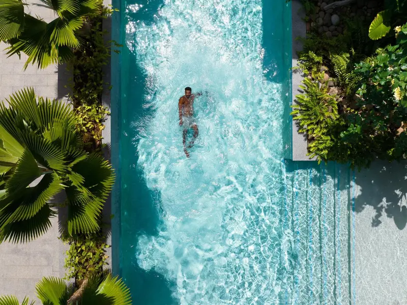 Une personne nage dans une piscine rectangulaire entourée de végétation tropicale.