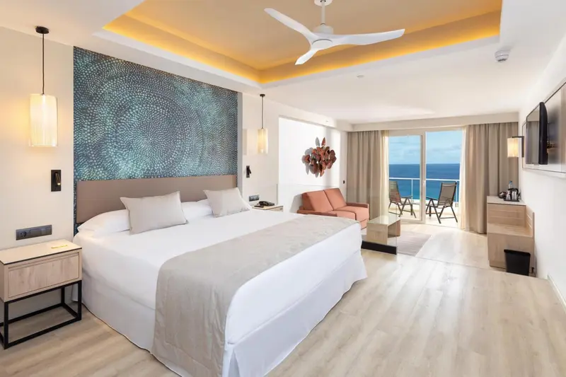 Chambre lumineuse avec un grand lit et un accès à une terrasse vue sur mer.