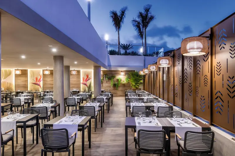 Une salle de restaurant lumineuse avec des tables dressées et une décoration tropicale.