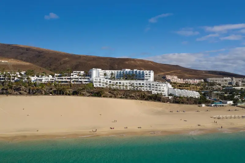 Vue aérienne d'un complexe hôtelier blanc bordant une plage de sable fin et une mer turquoise.