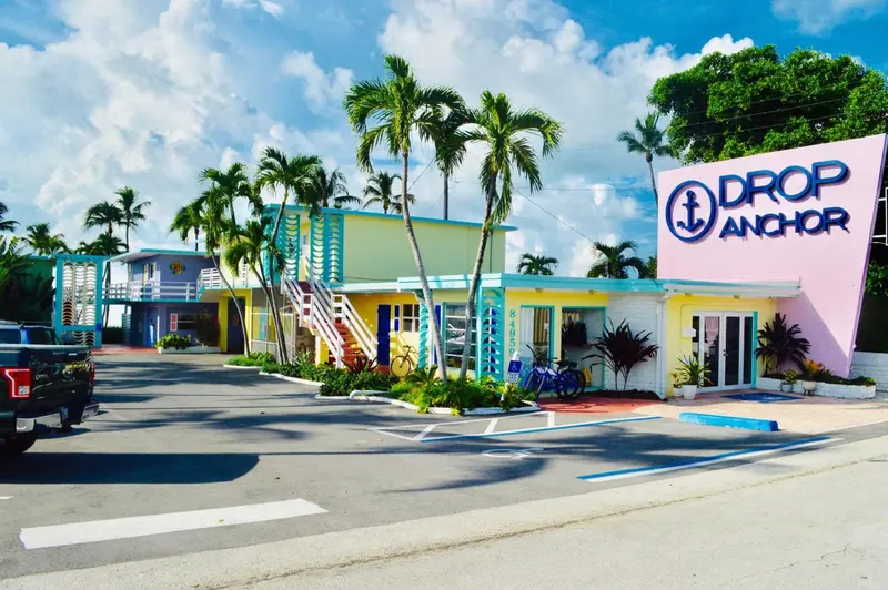 Bâtiment coloré avec une enseigne et des palmiers devant un parking.