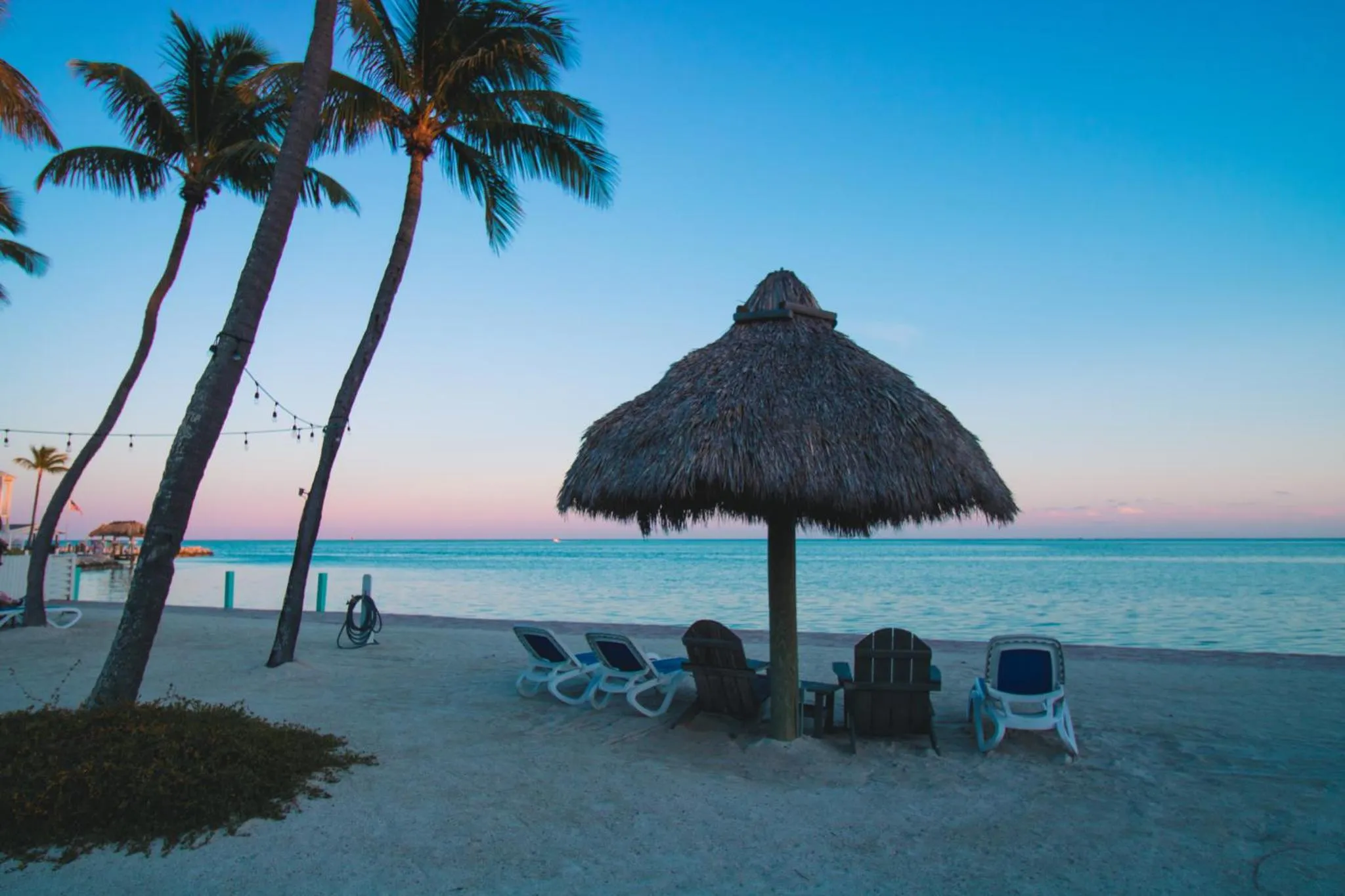 Transats et parasol sur une plage de sable blanc au coucher du soleil.