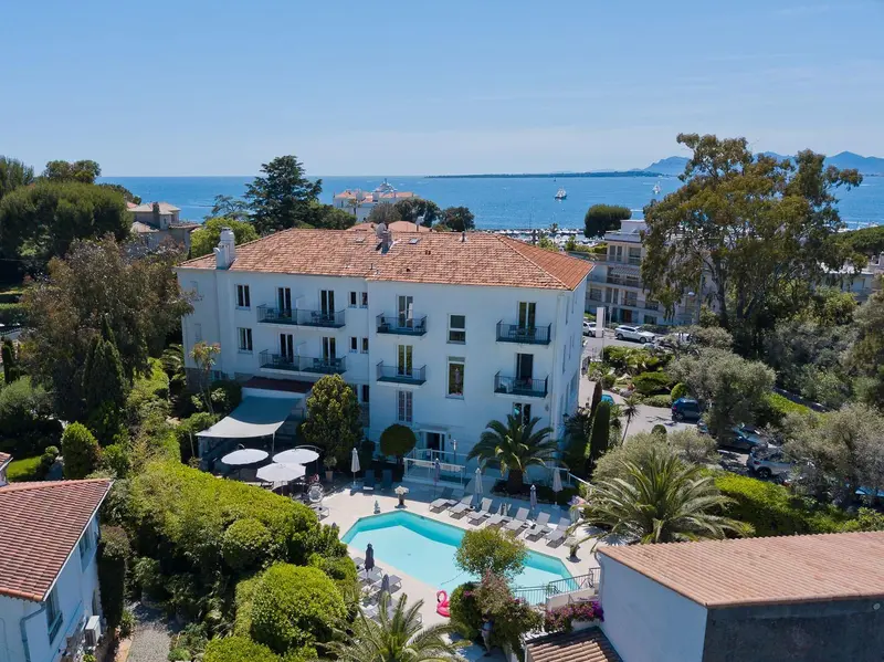 Bâtiment blanc à plusieurs étages avec piscine et végétation luxuriante en bord de mer.