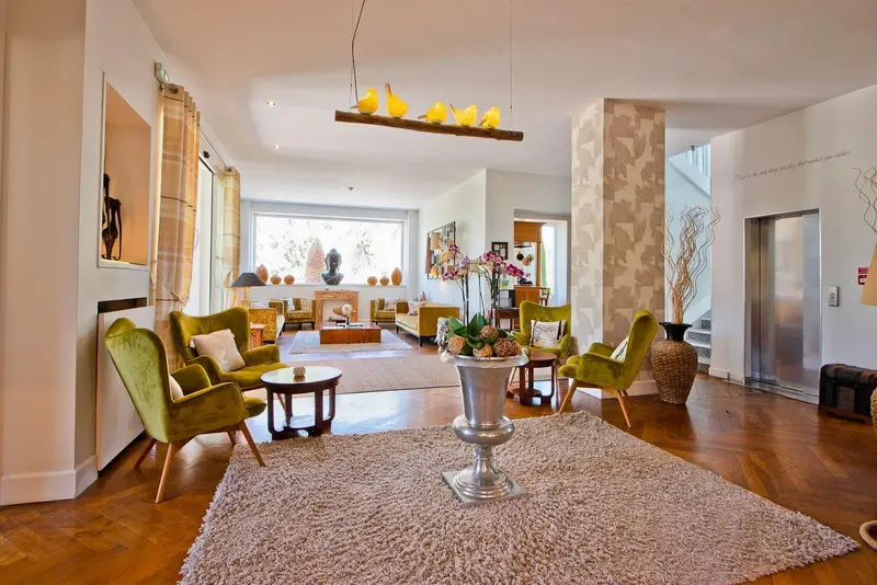 Un salon spacieux et lumineux avec des fauteuils verts et un tapis moelleux.