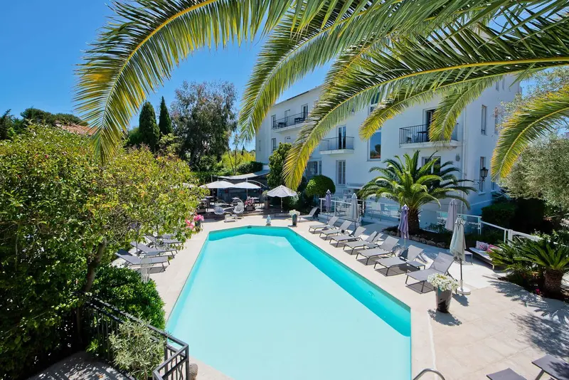 Piscine turquoise bordée de transats dans un jardin luxuriant.