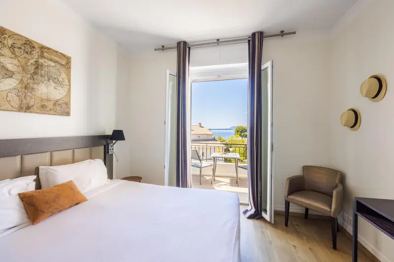Une chambre lumineuse s'ouvre sur un balcon avec vue sur la mer.