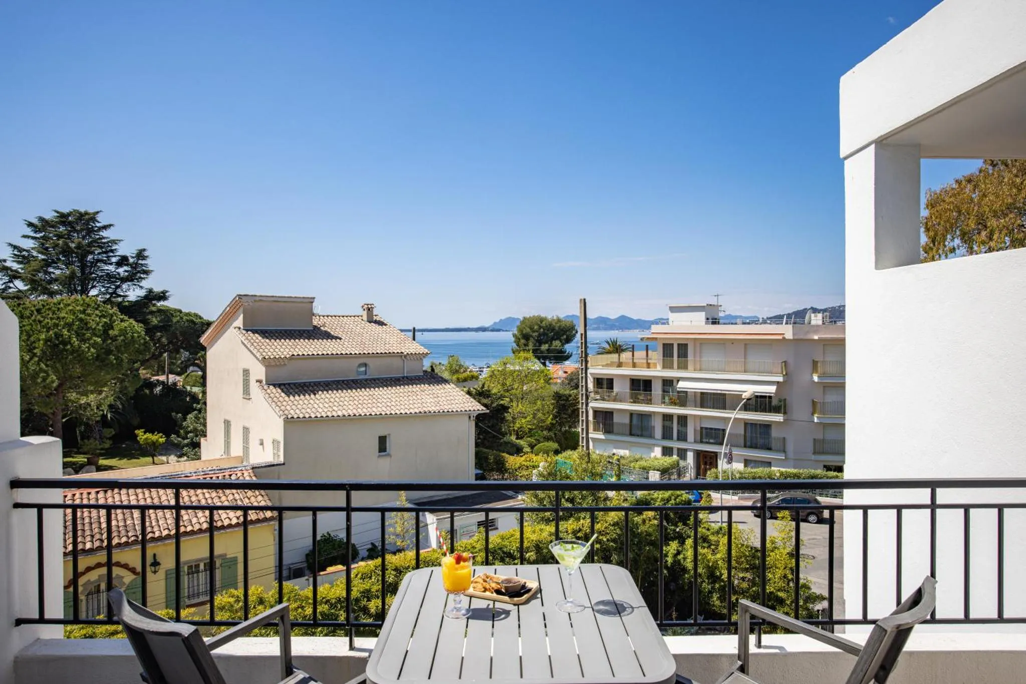 Une table avec des boissons et des en-cas est mise en scène sur un balcon avec vue sur la mer.