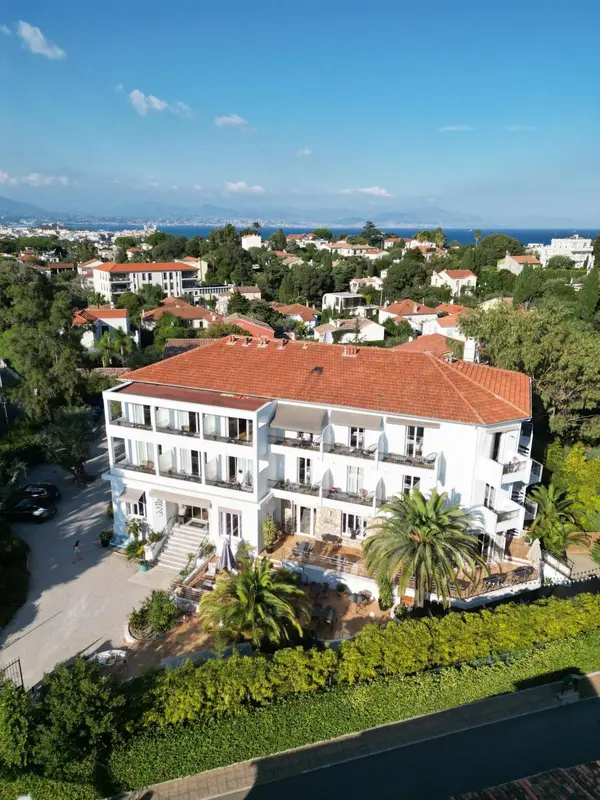 Vue aérienne d'un bâtiment blanc avec des toits en tuiles rouges et une végétation luxuriante.