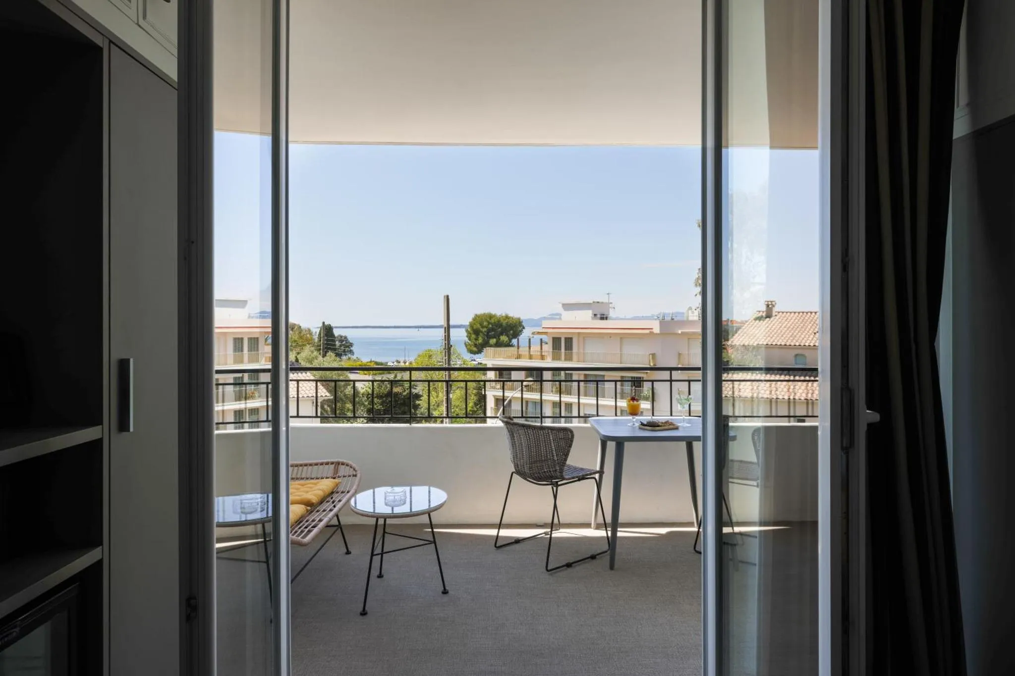 Une terrasse avec une table et des chaises offre une vue sur la mer et la végétation.