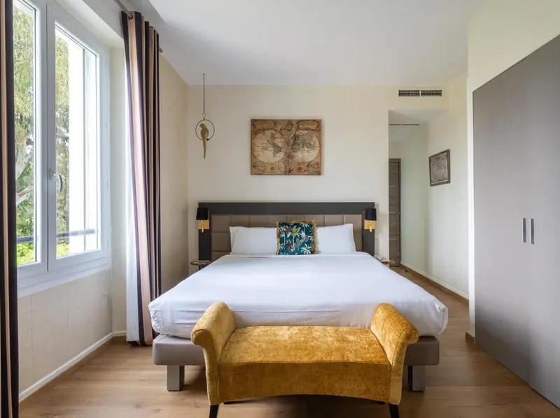 Une chambre lumineuse avec un grand lit et un banc jaune.