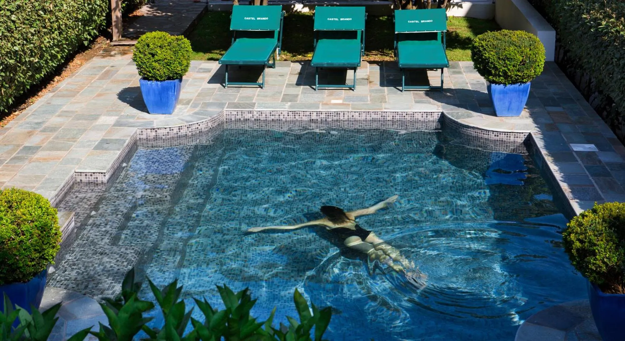 Une personne flotte sur le dos dans une piscine rectangulaire bordée d'une terrasse.