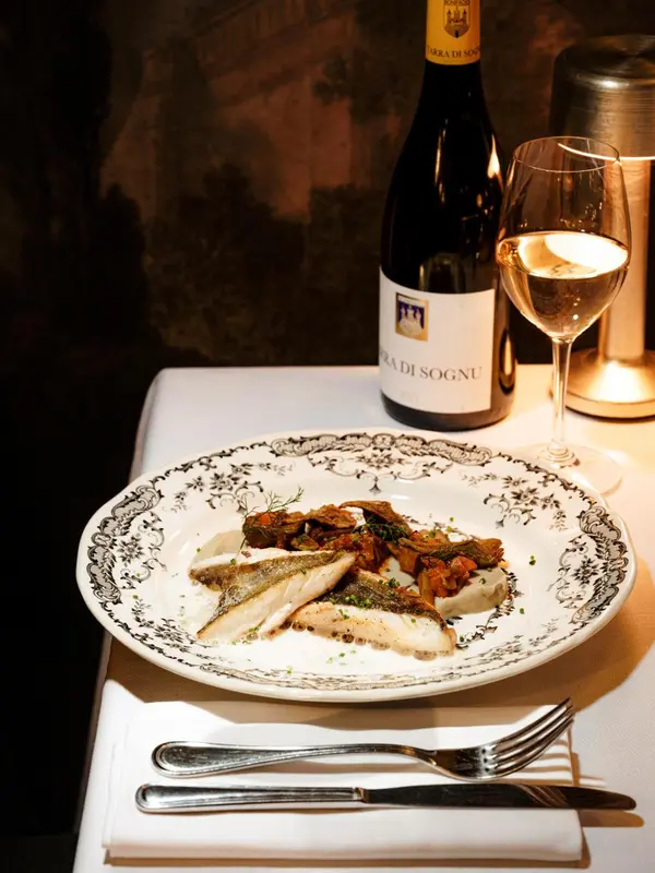 Une assiette de poisson est présentée avec une bouteille de vin et un verre sur une table nappée.