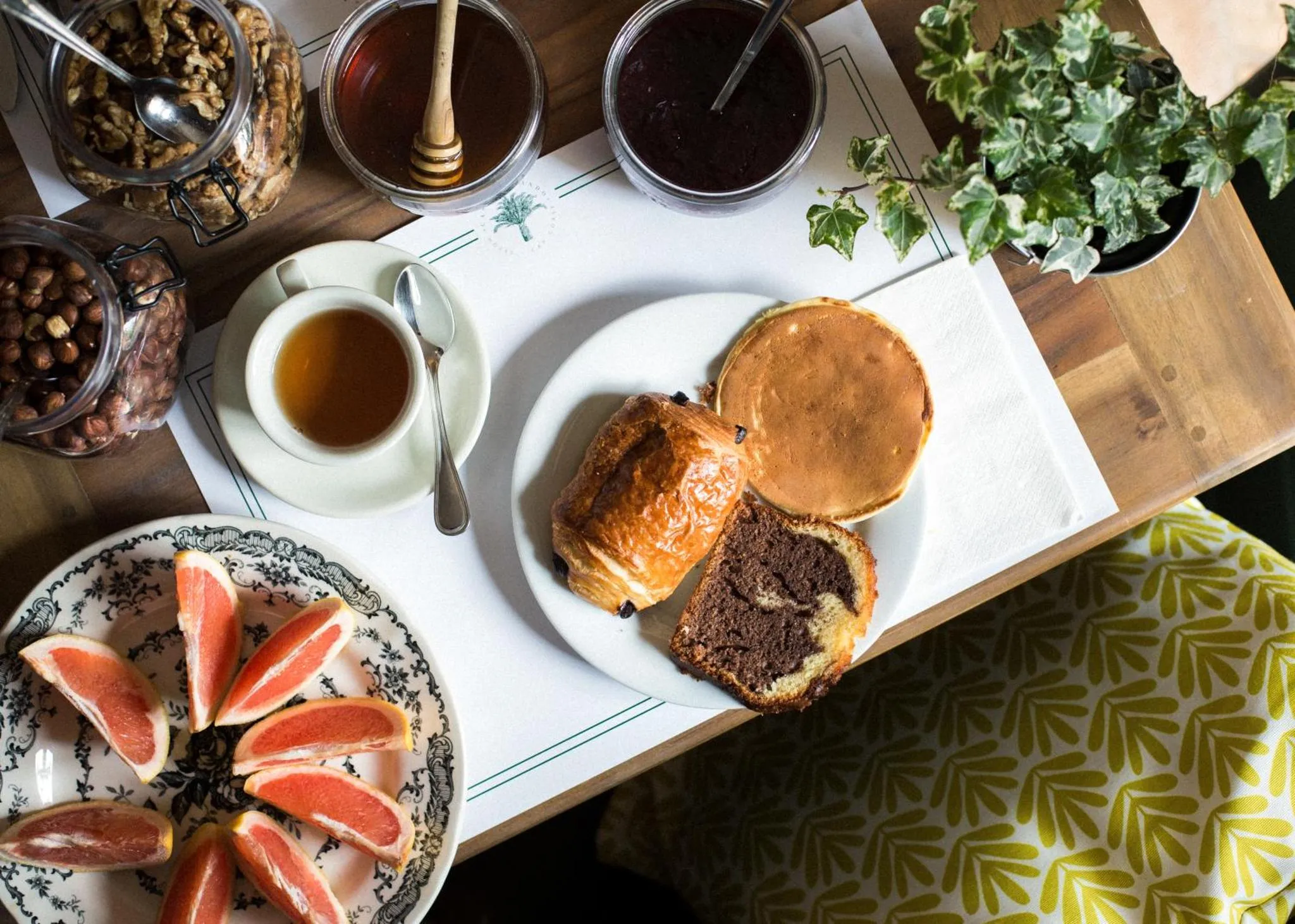 Un petit-déjeuner avec des céréales, des fruits, des viennoiseries et une boisson chaude est présenté sur une table.