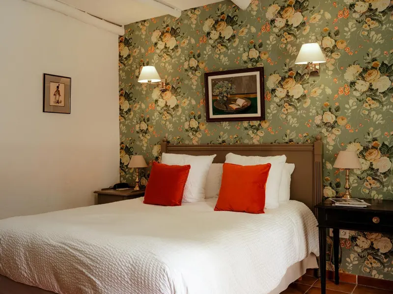 Une chambre lumineuse avec un lit recouvert d'une courtepointe blanche et de coussins orange.
