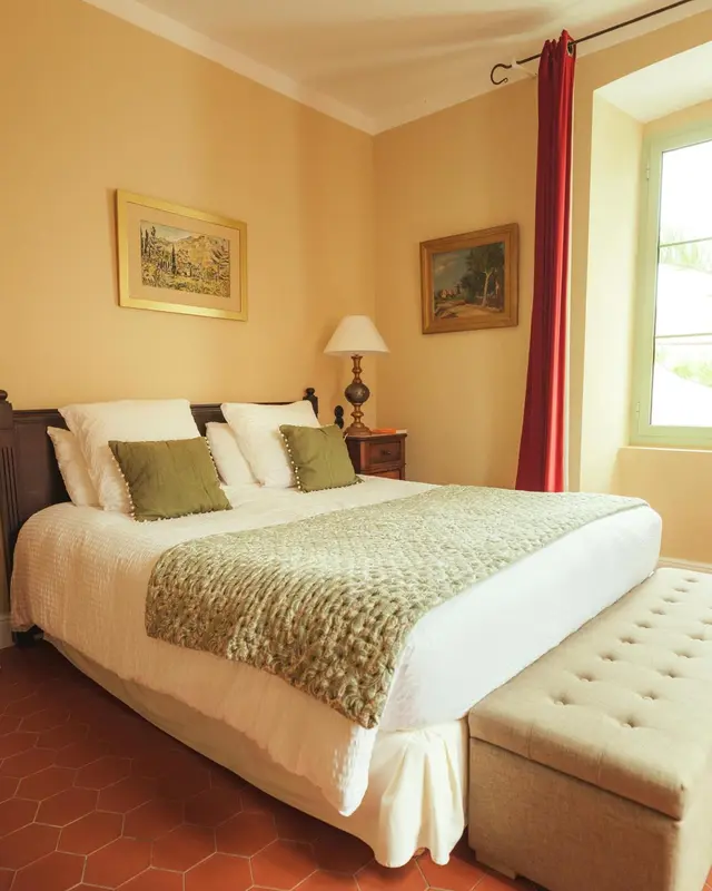 Une chambre lumineuse avec un lit recouvert d'une courtepointe et un banc au pied du lit.