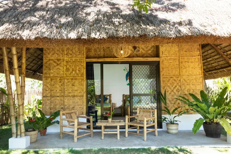 Une terrasse en bois devant une structure en bambou abrite des fauteuils et une petite table basse.