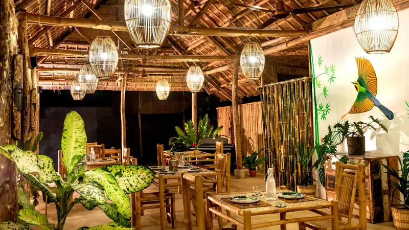 Une salle à manger en bois avec des tables et des chaises, éclairée par des suspensions en osier.