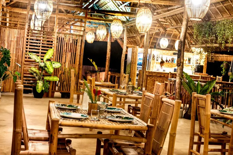 Une salle à manger en bois avec des tables dressées et des suspensions en rotin.