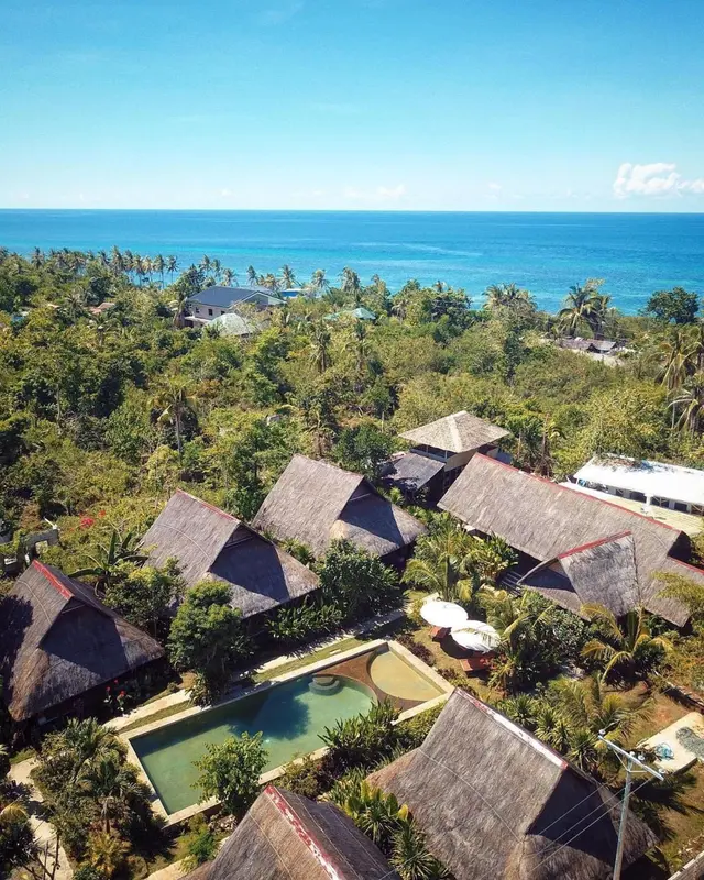 Vue aérienne d'un complexe hôtelier tropical avec piscine et végétation luxuriante.