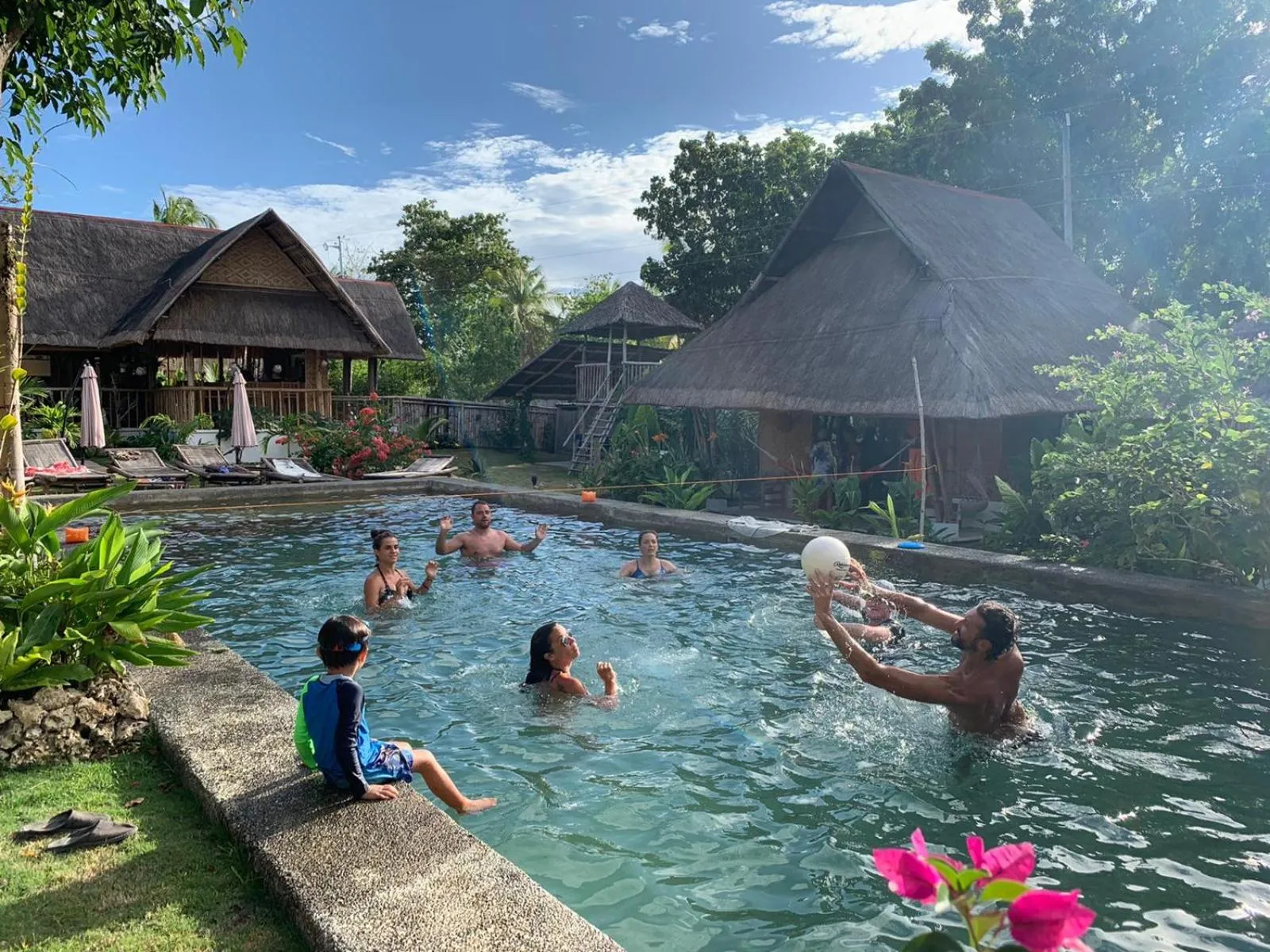 Des personnes se rafraîchissent dans une piscine ensoleillée entourée de végétation luxuriante.