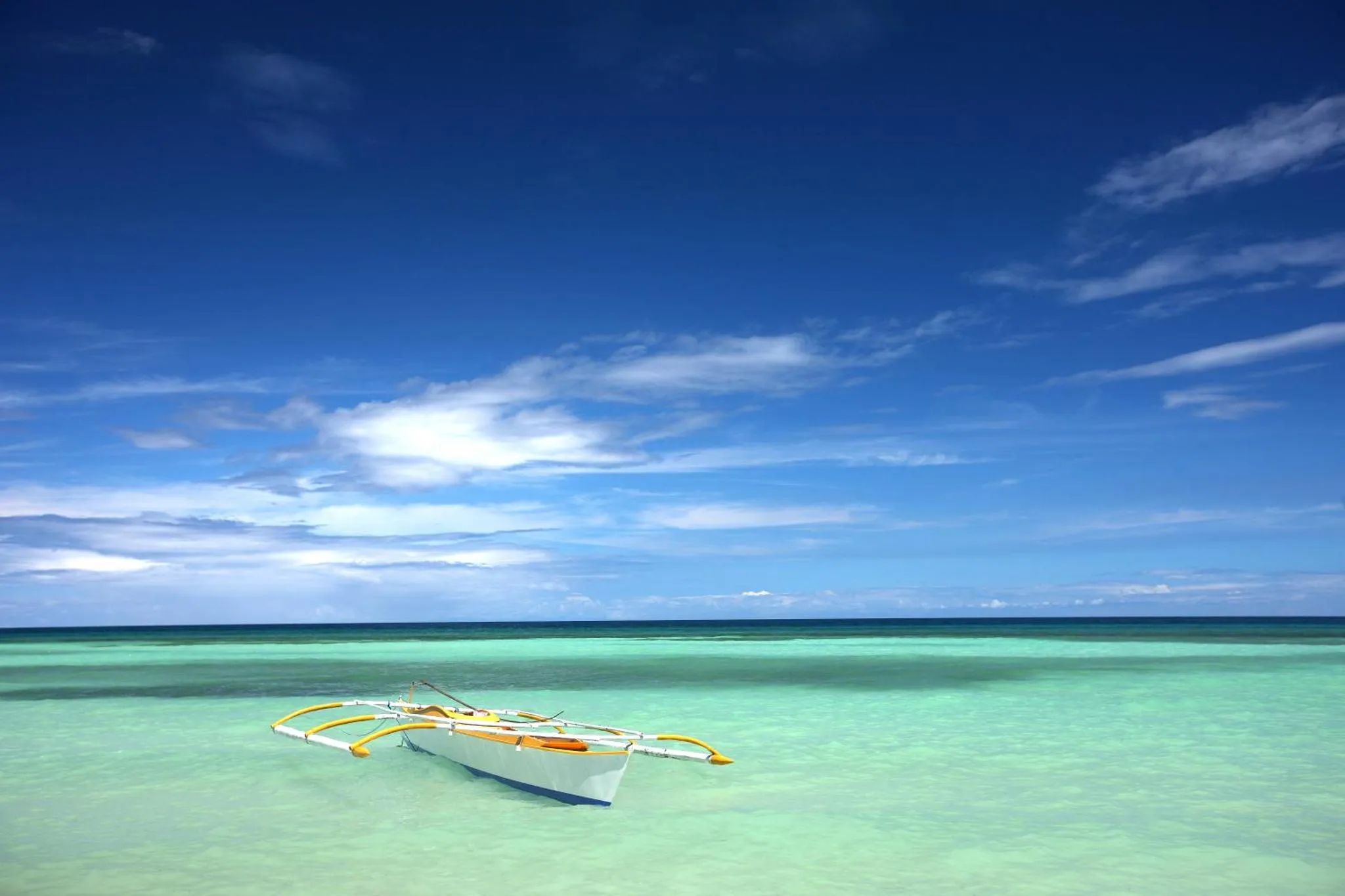 Un bateau de pêche traditionnel repose sur une eau turquoise et peu profonde sous un ciel bleu nuageux.