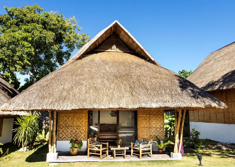 Petite maison de style tropical avec toit de chaume et terrasse.